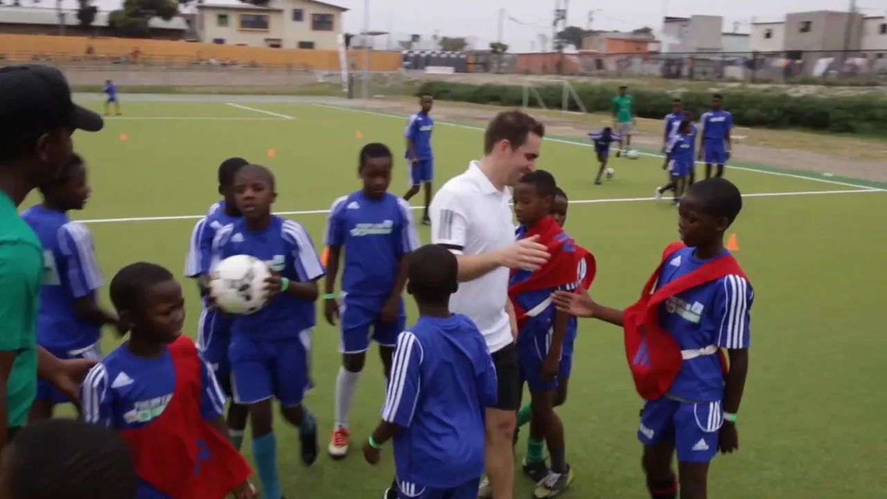 Philipp Lahm steht auf einem Fußballplatz zwischen Kindern in blauen Trikots