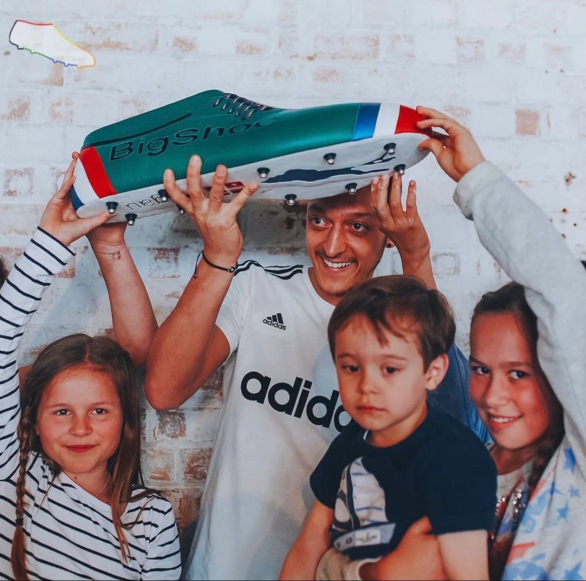Mesut Özil und drei Kinder heben einen BigShoe über ihre Köpfe